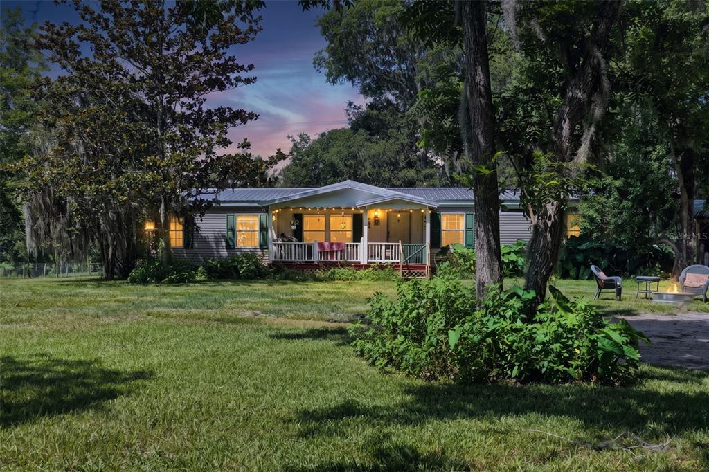 A single-story house with a front porch and string lights sits on a grassy lawn — 16242 NW 130TH STREET, WILLISTON, FL