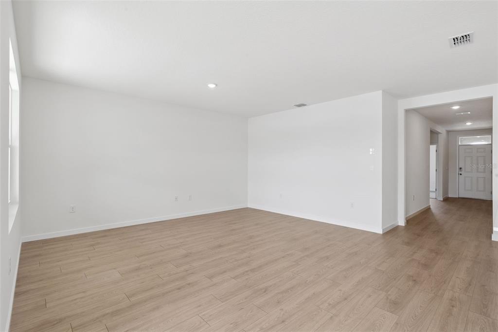 An empty room with light wood-look flooring and white walls leads to an entryway — 1024 CHAMPION RIDGE DRIVE, DAYTONA BEACH, FL