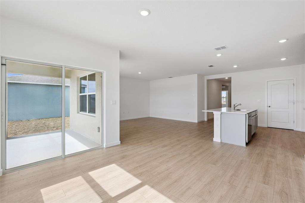 An open-concept room with light wood-look flooring, a kitchen island, and a sliding glass door — 1024 CHAMPION RIDGE DRIVE, DAYTONA BEACH, FL