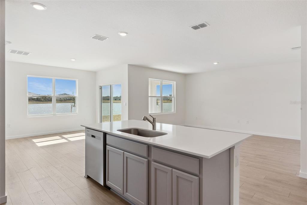 A kitchen island with a stainless steel sink and dishwasher faces a bright, open-concept room — 1024 CHAMPION RIDGE DRIVE, DAYTONA BEACH, FL