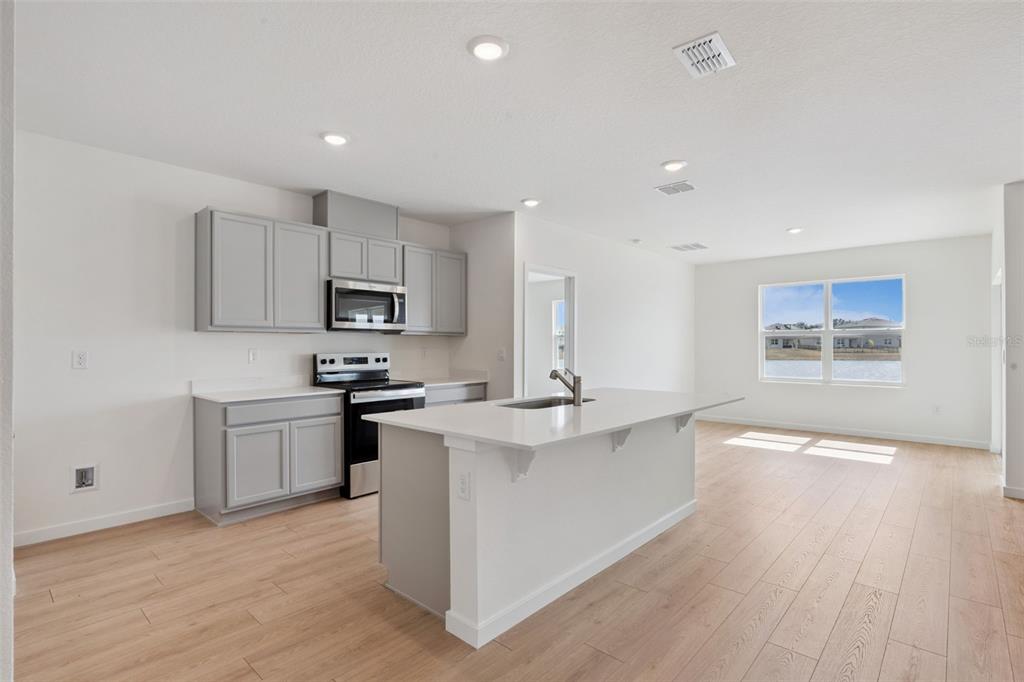 A modern kitchen features gray cabinets, stainless steel appliances, a white island, and light flooring — 1024 CHAMPION RIDGE DRIVE, DAYTONA BEACH, FL