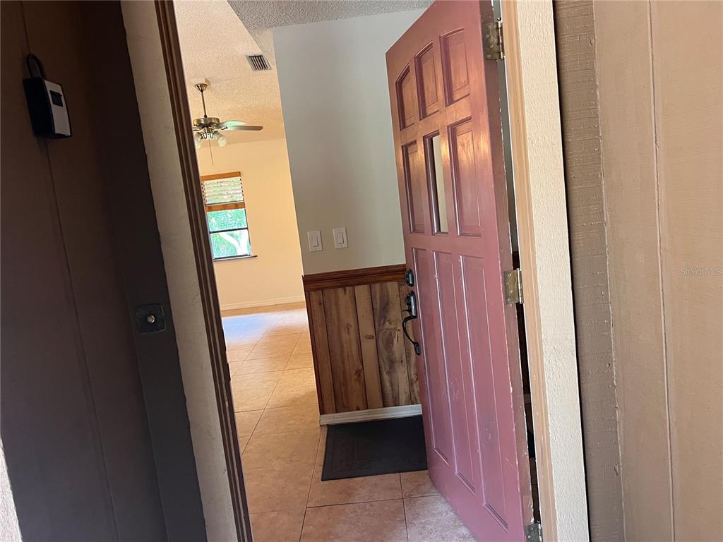 An open pink front door reveals an interior with tile flooring and wood-paneled walls — 2919 NICHOLAS ROAD, FORT PIERCE, FL