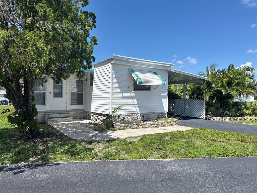 A white mobile home features a carport, a small concrete patio, and a metal awning — 7164 MOUNT GEORGETOWN DRIVE NE UNIT 553, ST PETERSBURG, FL