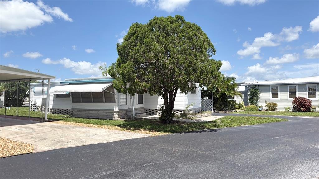 A white mobile home with a large tree in the front yard and a carport — 7164 MOUNT GEORGETOWN DRIVE NE UNIT 553, ST PETERSBURG, FL