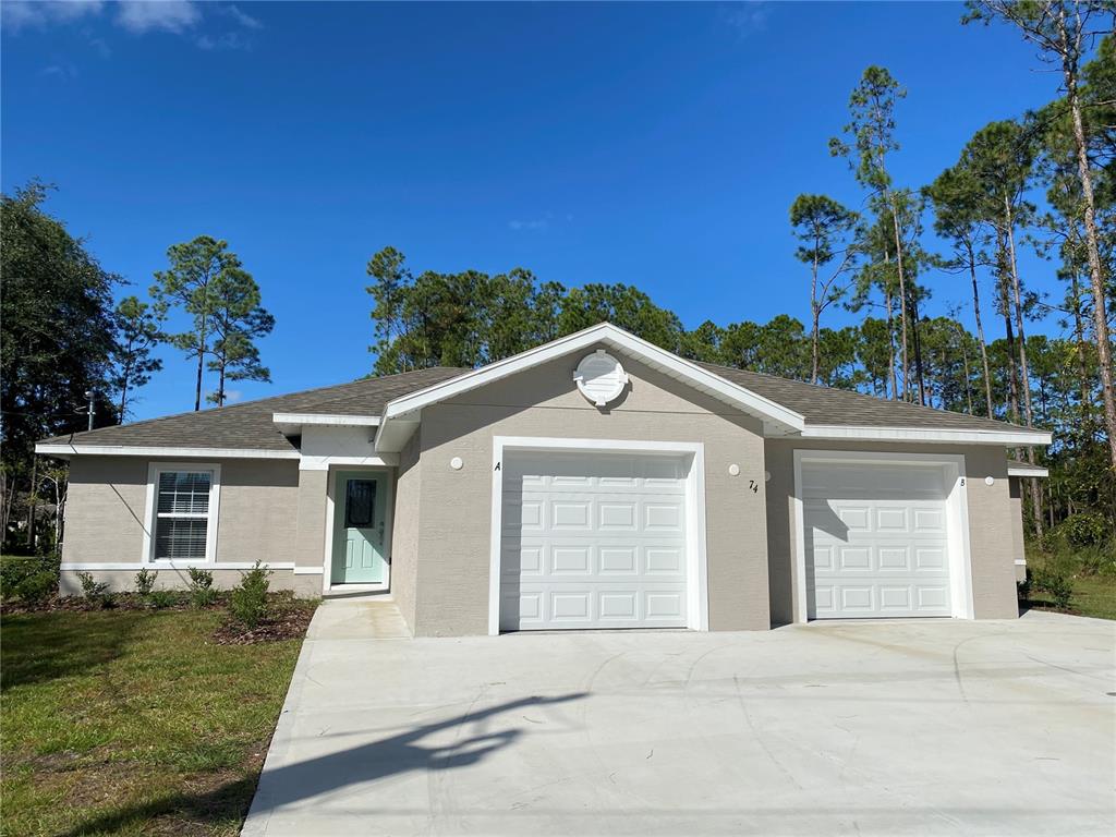 A single-story duplex with two garage doors, beige stucco siding, and a concrete driveway — 74 EMERSON DRIVE UNIT A & B, PALM COAST, FL