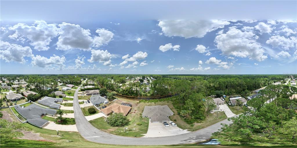 A view of a grassy backyard with trees, a small pond, and a house exterior — 74 EMERSON DRIVE UNIT A & B, PALM COAST, FL