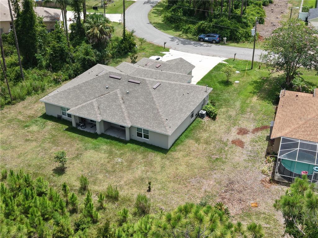 A grassy backyard overlooks a small pond bordered by a line of tall pine trees — 74 EMERSON DRIVE UNIT A & B, PALM COAST, FL