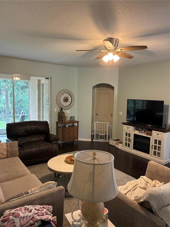 A living room features a ceiling fan, dark wood floors, a television console, and seating — 8872 FOUNDERS CIRCLE, PALMETTO, FL