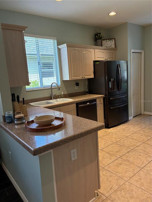 A kitchen features light wood cabinets, granite countertops, a black refrigerator, and tile flooring — 8872 FOUNDERS CIRCLE, PALMETTO, FL