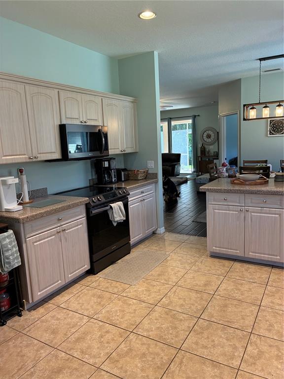 A kitchen features light wood cabinets, black appliances, and tile flooring, opening into a dining area — 8872 FOUNDERS CIRCLE, PALMETTO, FL