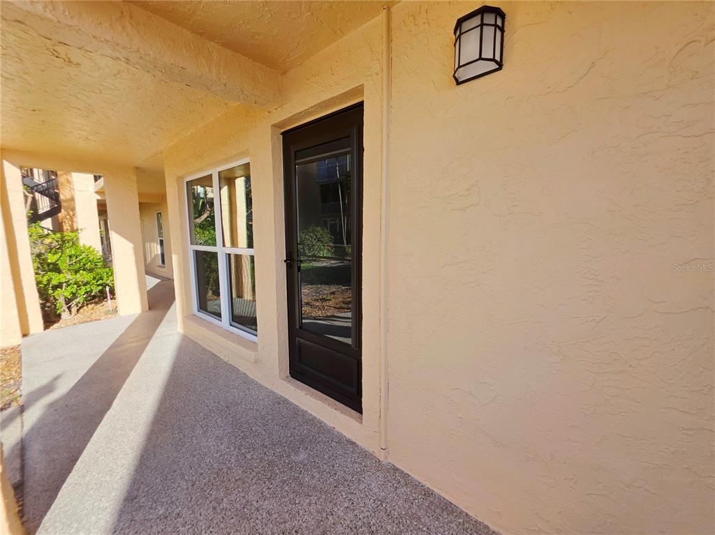 A covered walkway leads to a dark-framed glass door and a window on a building — 8921 BLIND PASS ROAD UNIT 142, ST PETE BEACH, FL