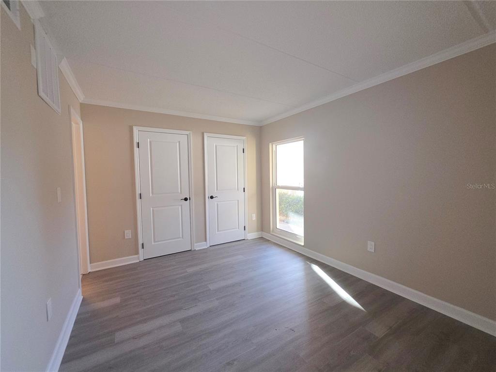 An empty room features light gray wood-look flooring, beige walls, two white doors, and a window — 8921 BLIND PASS ROAD UNIT 142, ST PETE BEACH, FL