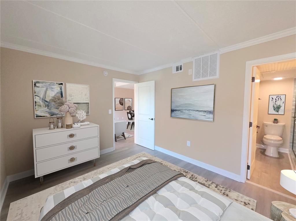 A bedroom with a white dresser, a bed, and an open doorway leading to a bathroom — 8921 BLIND PASS ROAD UNIT 142, ST PETE BEACH, FL