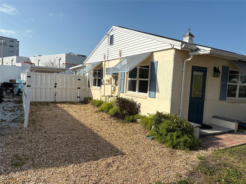 A side view of a light-colored house with blue shutters and a gravel yard — 111 174TH AVENUE E, REDINGTON SHORES, FL
