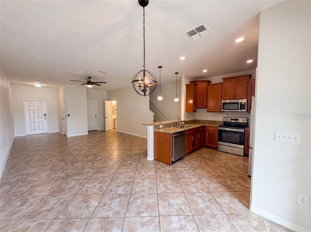 An open-concept kitchen and living area features tile flooring, wood cabinets, and a pendant light — 13717 ROSETTE ROAD, HUDSON, FL