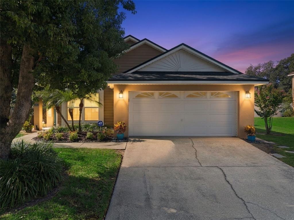 A single-story house with a white garage door, tan siding, and a concrete driveway at dusk — 1038 ROYAL OAKS DRIVE, APOPKA, FL