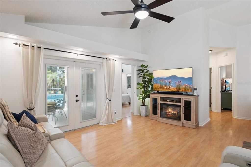A living room with light wood floors, a fireplace console, and glass doors to a patio — 1038 ROYAL OAKS DRIVE, APOPKA, FL