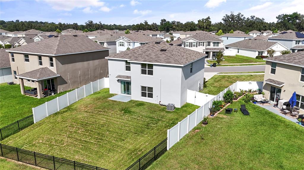 An aerial view shows the backyard of a two-story house with a white vinyl fence — 13695 WINEBERRY DRIVE, DADE CITY, FL