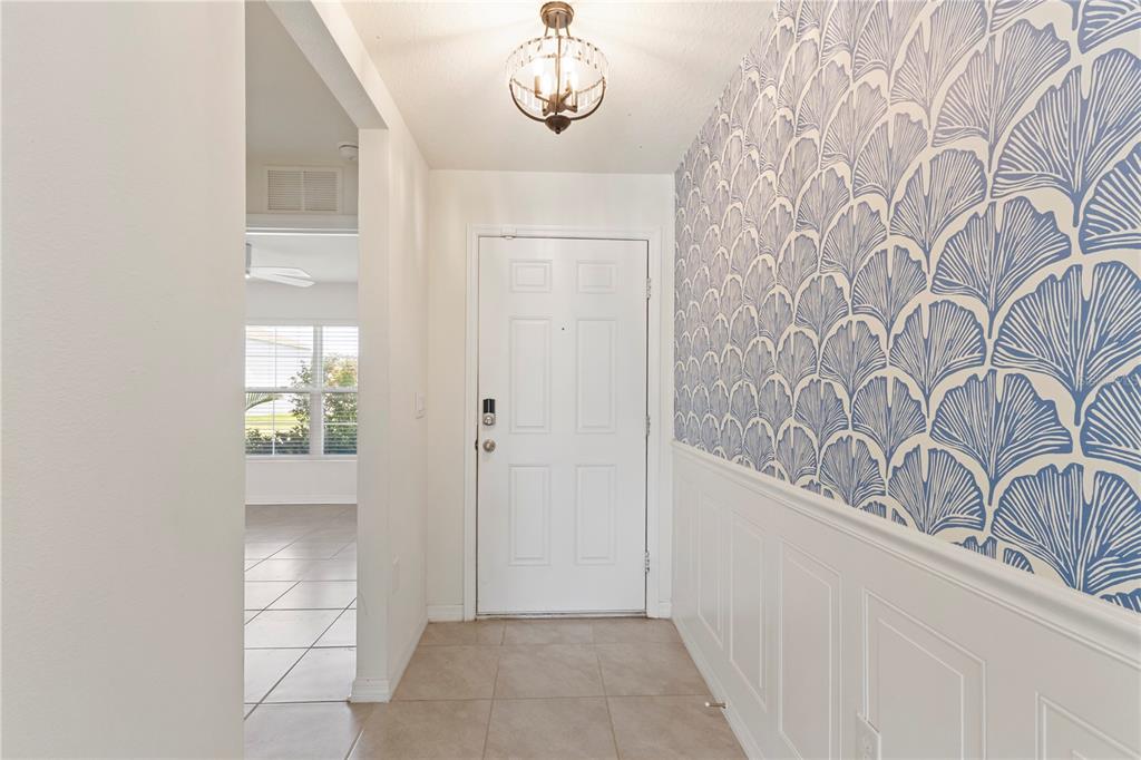 An entryway features a white door, tiled floor, and a wall with blue ginkgo wallpaper — 13695 WINEBERRY DRIVE, DADE CITY, FL