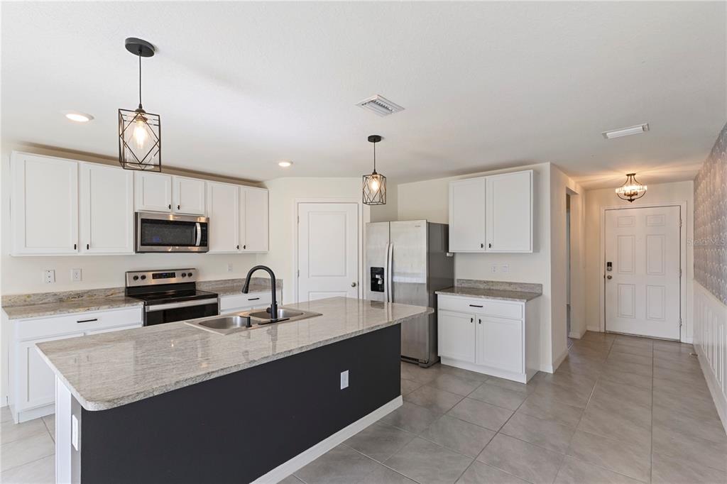 A kitchen with white cabinets, granite countertops, a dark island, and stainless steel appliances — 13695 WINEBERRY DRIVE, DADE CITY, FL
