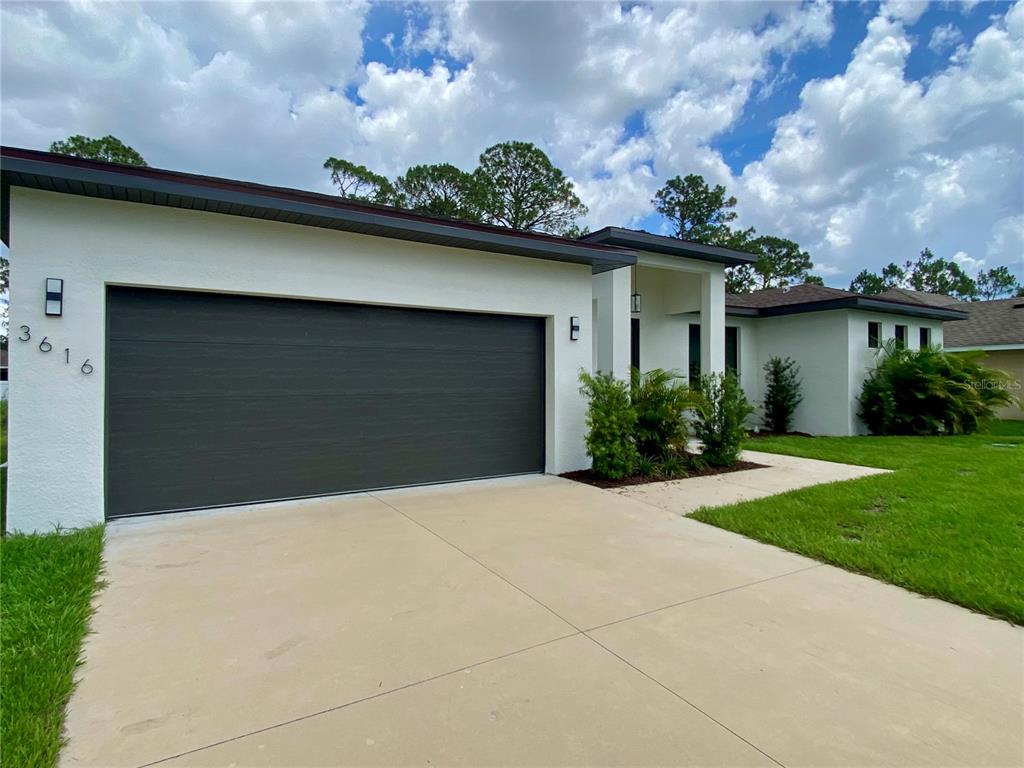 A single-story house with a white stucco exterior, a dark garage door, and a concrete driveway — 3616 BELLEFONTE AVENUE, NORTH PORT, FL