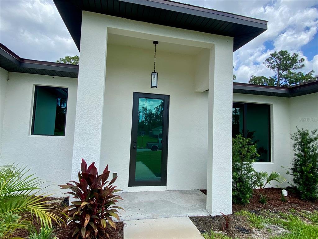 The exterior entrance features a white stucco facade, a dark framed glass door, and landscaping — 3616 BELLEFONTE AVENUE, NORTH PORT, FL