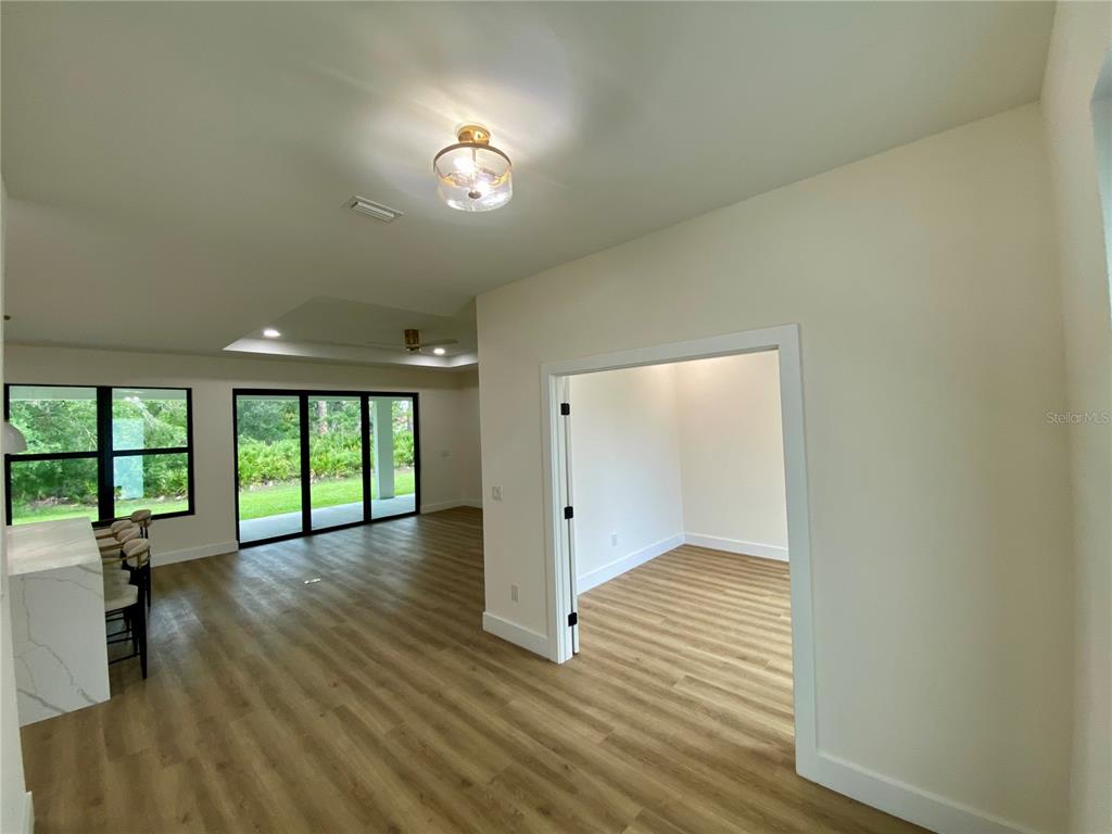 A bright living area with wood-look flooring leads to a separate room through a doorway — 3616 BELLEFONTE AVENUE, NORTH PORT, FL