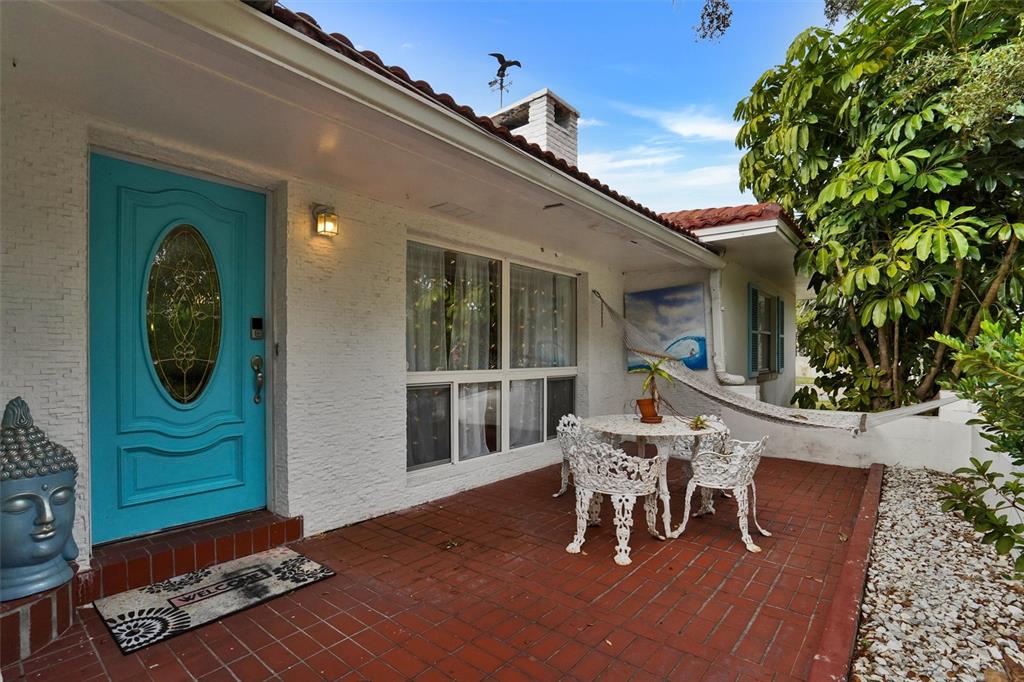 A red brick patio features a white bistro set, a hammock, and a turquoise front door — 7716 DARTMOUTH AVENUE N, ST PETERSBURG, FL