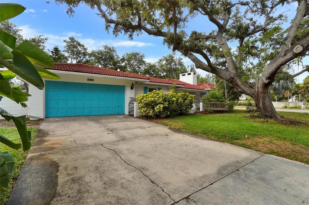 A single-story house with a turquoise garage door, red tile roof, and a large tree — 7716 DARTMOUTH AVENUE N, ST PETERSBURG, FL