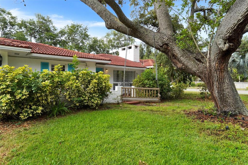 A white house with a red tile roof features a wooden swing under a tree — 7716 DARTMOUTH AVENUE N, ST PETERSBURG, FL
