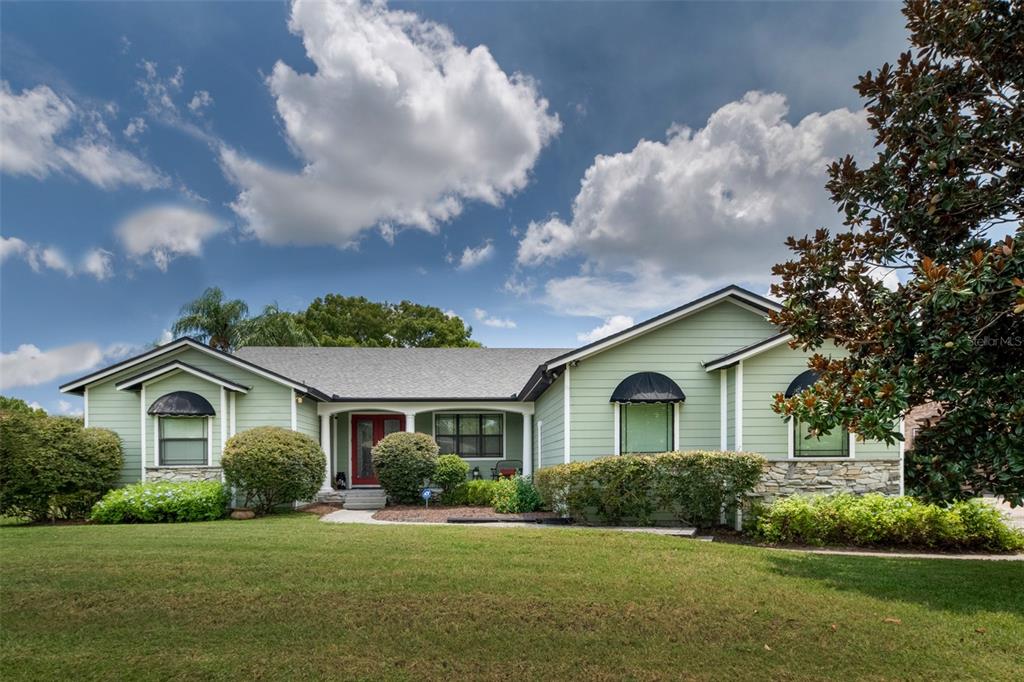 A light green single-story house features a red front door and black window awnings — 834 MILLSHORE DRIVE, CHULUOTA, FL