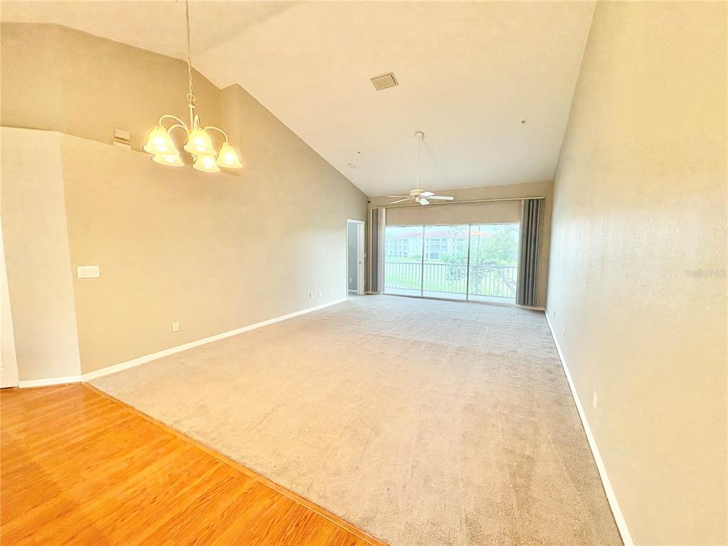 A spacious living room features vaulted ceilings, beige carpeting, a chandelier, and a sliding glass door — 6554 FAIRWAY GARDENS DRIVE UNIT 6554, BRADENTON, FL