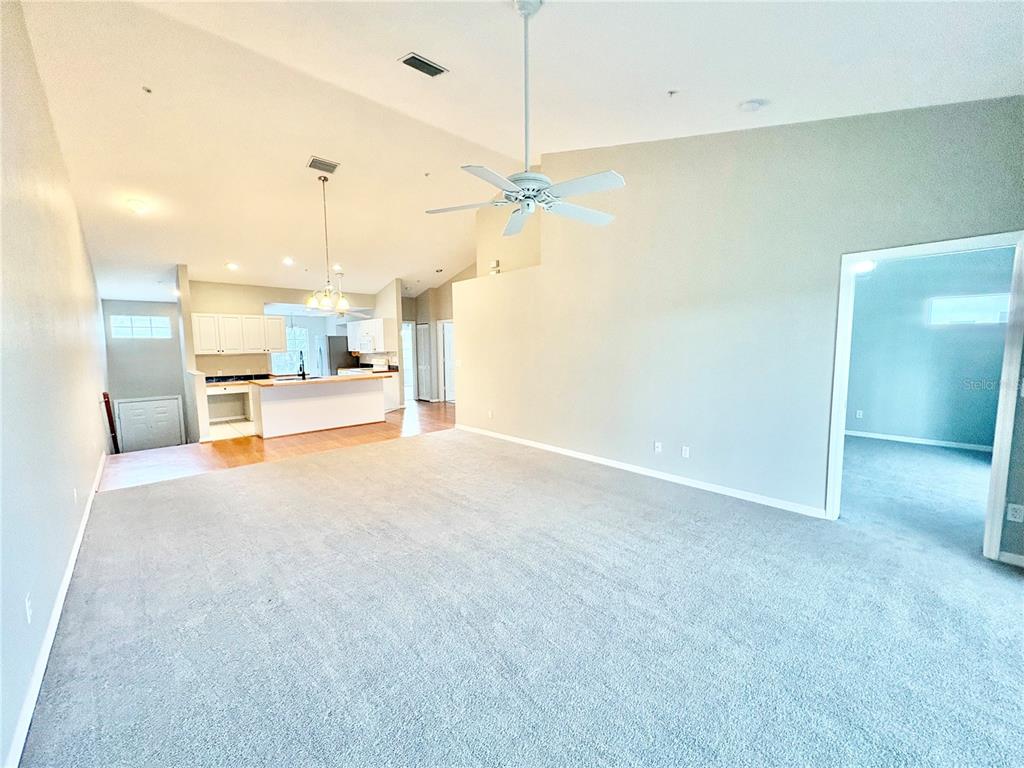 A spacious living room with gray carpet leads to an open kitchen with white cabinets — 6554 FAIRWAY GARDENS DRIVE UNIT 6554, BRADENTON, FL