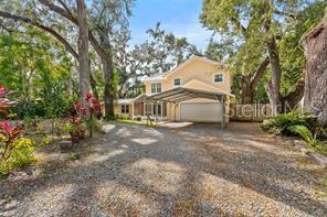 A two-story house with a metal carport sits on a gravel driveway surrounded by trees — 315 WOOTEN ROAD, LUTZ, FL