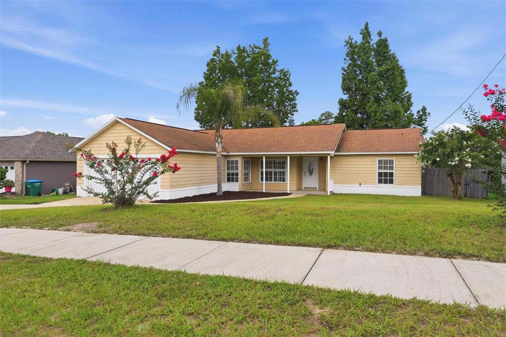 A beige house exterior features a covered front porch, white door, and a concrete walkway — 2695 KEENE LANE, DELTONA, FL