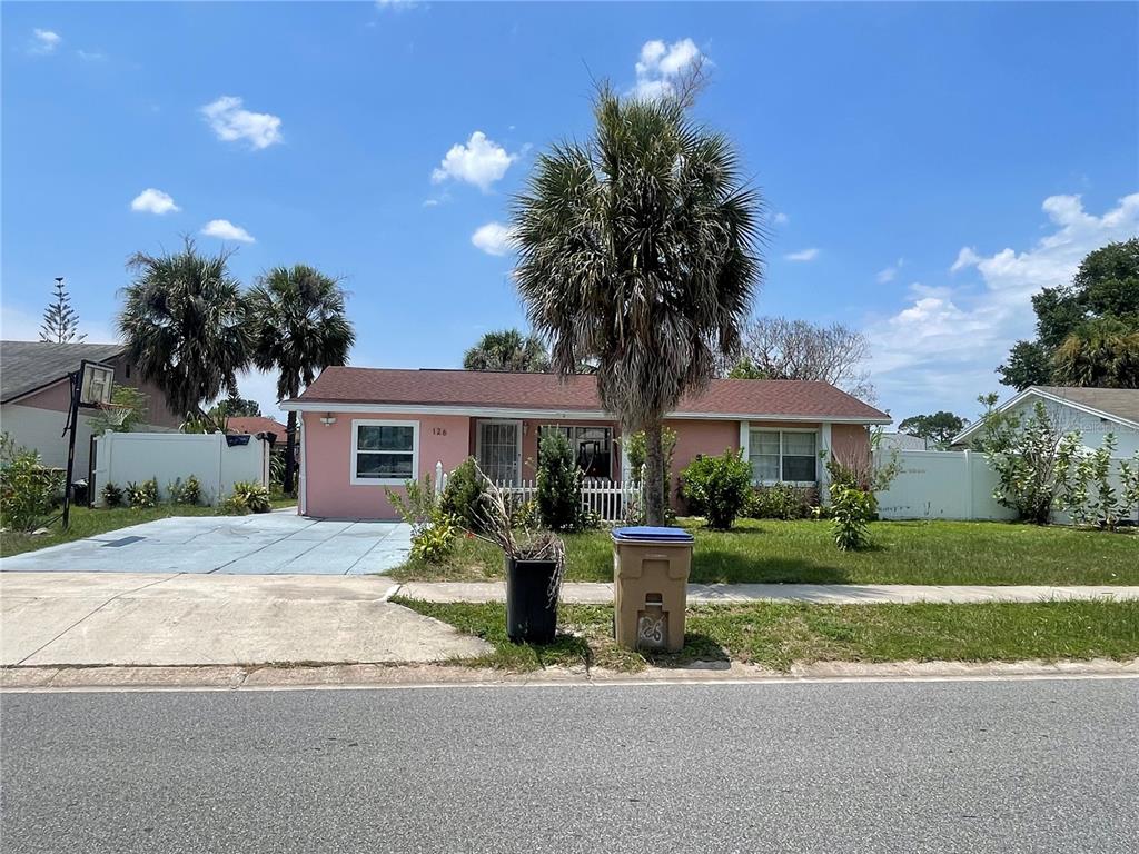 A single-story pink house with a palm tree in the front yard under a blue sky — 126 DAHLIA DRIVE, KISSIMMEE, FL