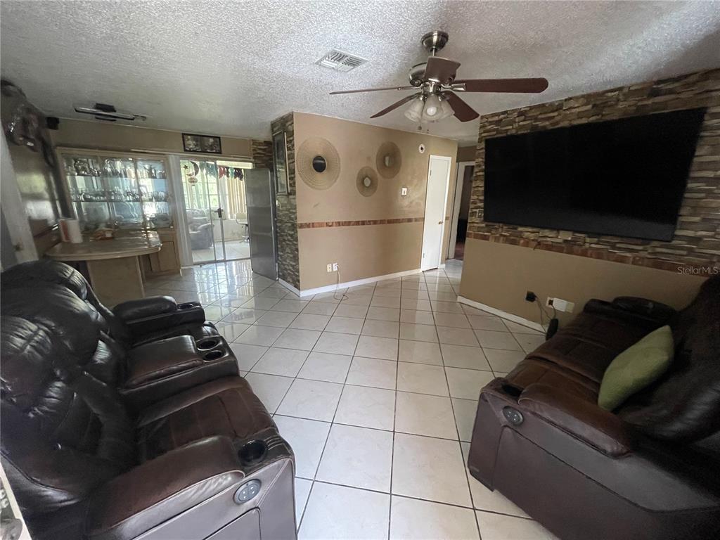 A living room features tile flooring, a stone accent wall with a television, and leather sofas — 126 DAHLIA DRIVE, KISSIMMEE, FL