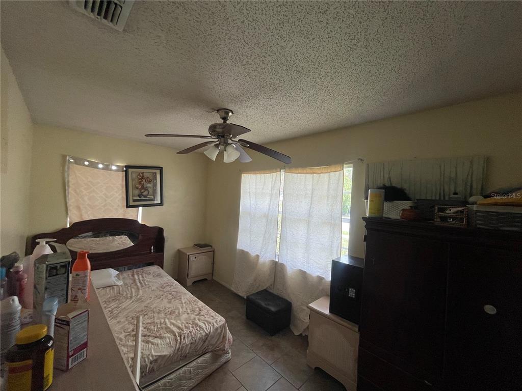 A bedroom features a bed, a ceiling fan, tiled floors, and a large dark cabinet — 126 DAHLIA DRIVE, KISSIMMEE, FL