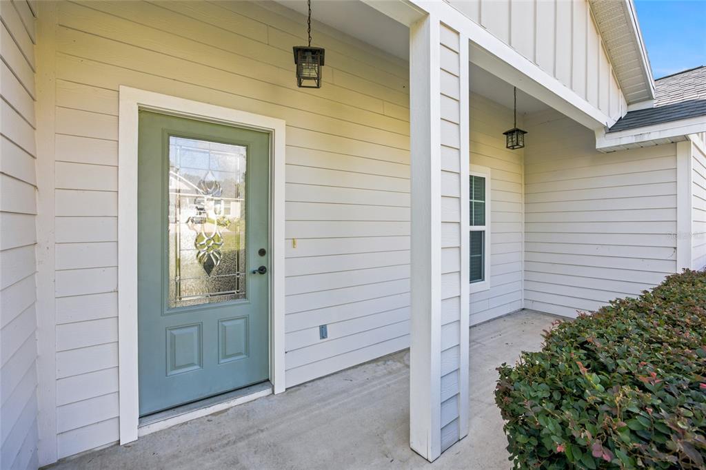 A covered front porch features light-colored horizontal siding, a sage green front door, and landscaping — 831 NE 150TH AVENUE, WILLISTON, FL