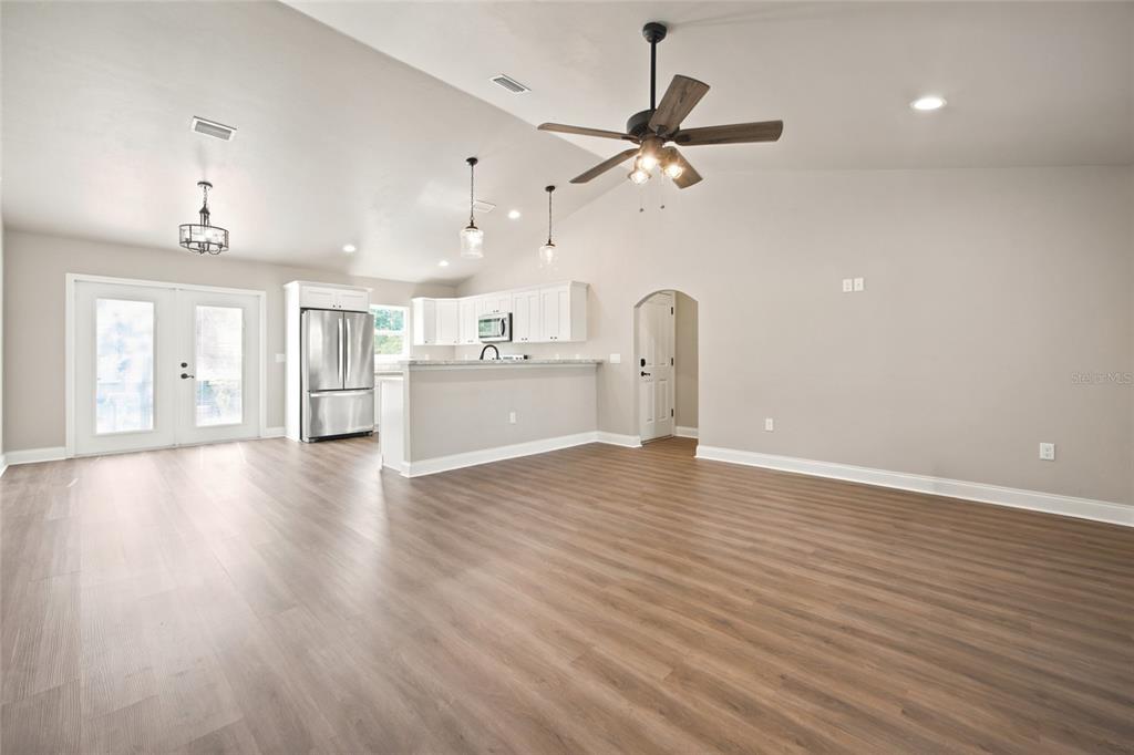 An open-concept living area features light wood-look flooring, a kitchen with white cabinets, and vaulted ceilings — 831 NE 150TH AVENUE, WILLISTON, FL