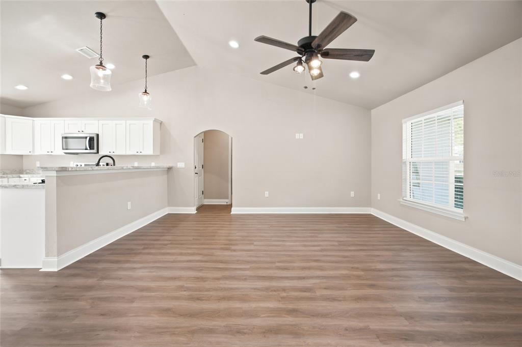 An open-concept living room with wood-look flooring, a vaulted ceiling, and an adjoining kitchen — 831 NE 150TH AVENUE, WILLISTON, FL