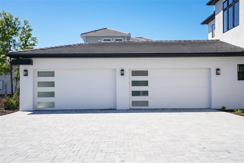 A white house exterior features two modern garage doors with horizontal frosted glass panels — 16000 PENDIO DRIVE, BELLA COLLINA, FL