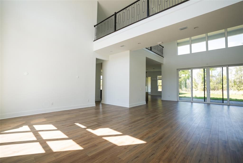 A spacious, high-ceilinged living area features light wood-look flooring and a second-story balcony railing — 16000 PENDIO DRIVE, BELLA COLLINA, FL