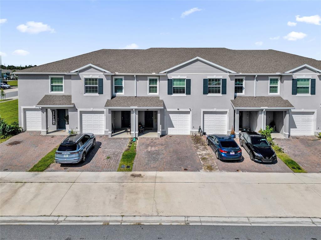 An exterior view of a multi-unit townhouse complex with gray siding and paved driveways — 1359 ISLETA LOOP, KISSIMMEE, FL