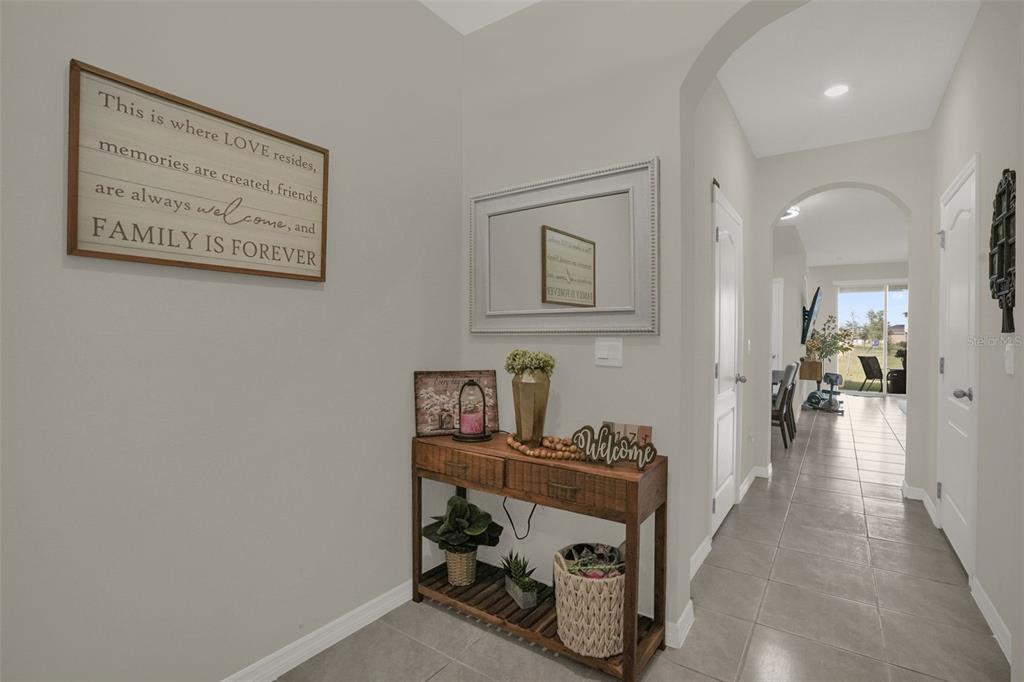 A tiled entryway features a wooden console table, wall decor, and a hallway leading outside — 1359 ISLETA LOOP, KISSIMMEE, FL