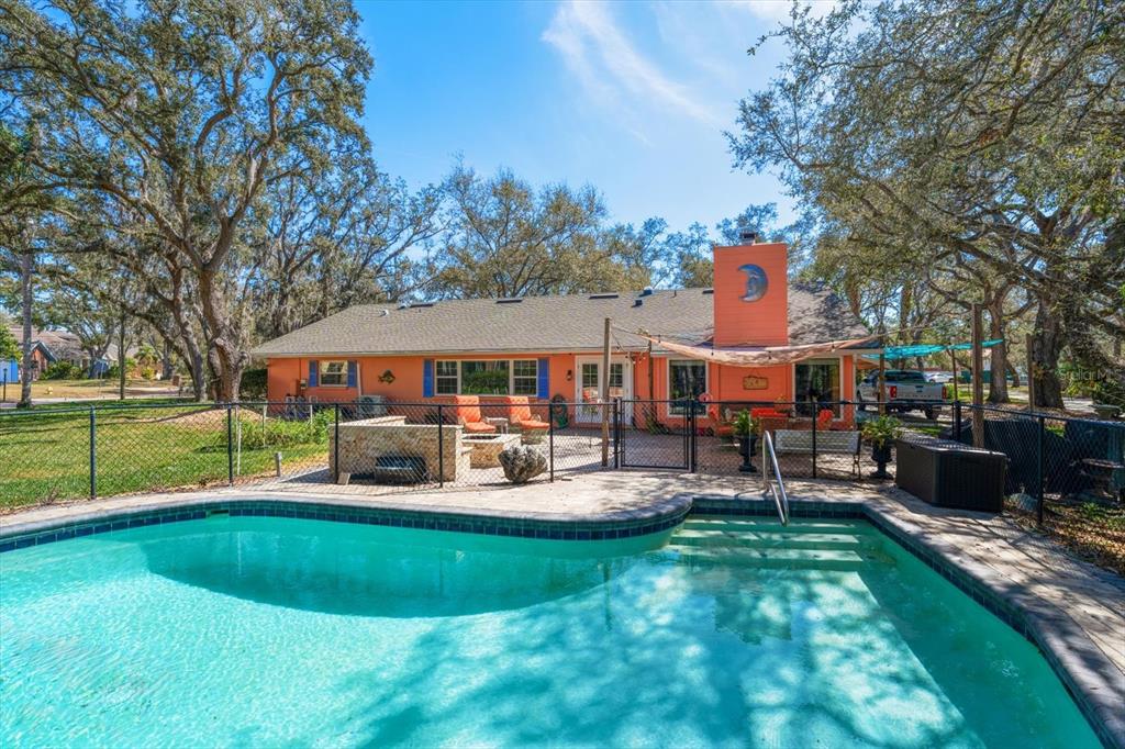 A backyard features a swimming pool with steps, a patio, and an orange house exterior — 1921 CARDINAL ROAD, DUNEDIN, FL