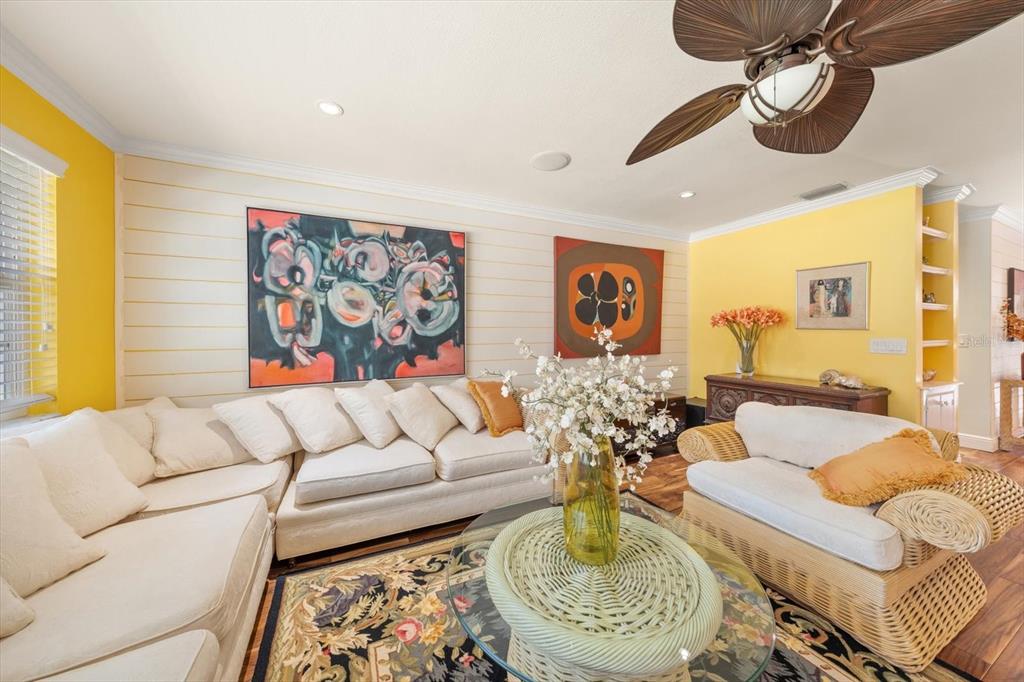 A living room features yellow walls, shiplap paneling, white sofas, and a ceiling fan — 1921 CARDINAL ROAD, DUNEDIN, FL