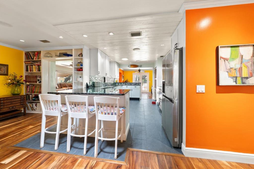 A kitchen with white cabinets, a dark island, and orange walls features wood flooring — 1921 CARDINAL ROAD, DUNEDIN, FL