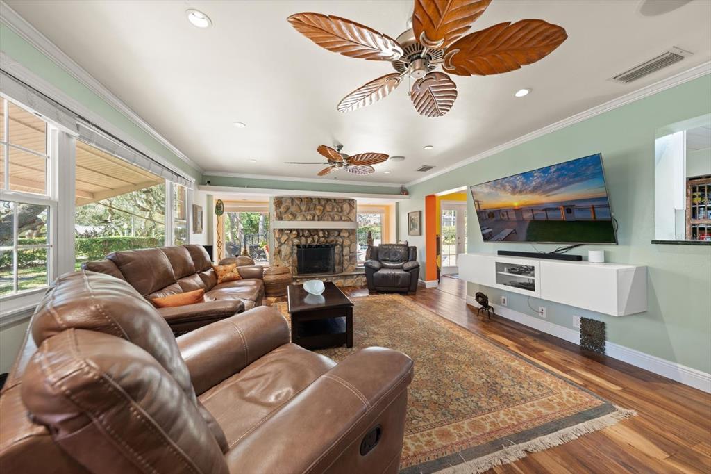 A living room features a stone fireplace, leather sofas, a television, and two ceiling fans — 1921 CARDINAL ROAD, DUNEDIN, FL