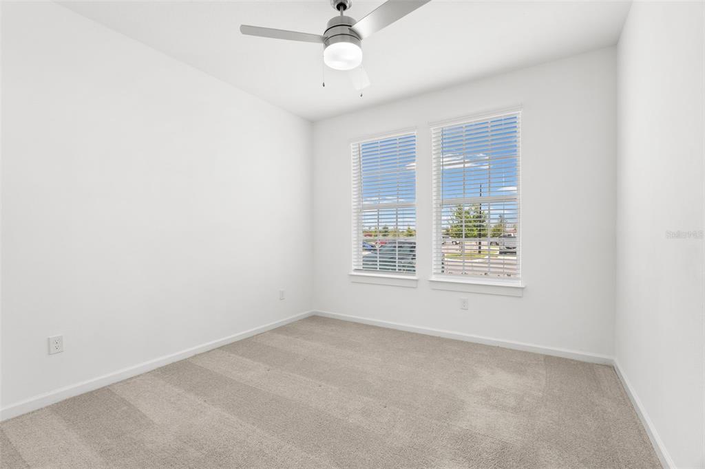 An empty bedroom features white walls, beige carpet, a ceiling fan, and two windows — 1700 RANCH ROAD UNIT A3-2116, NOKOMIS, FL
